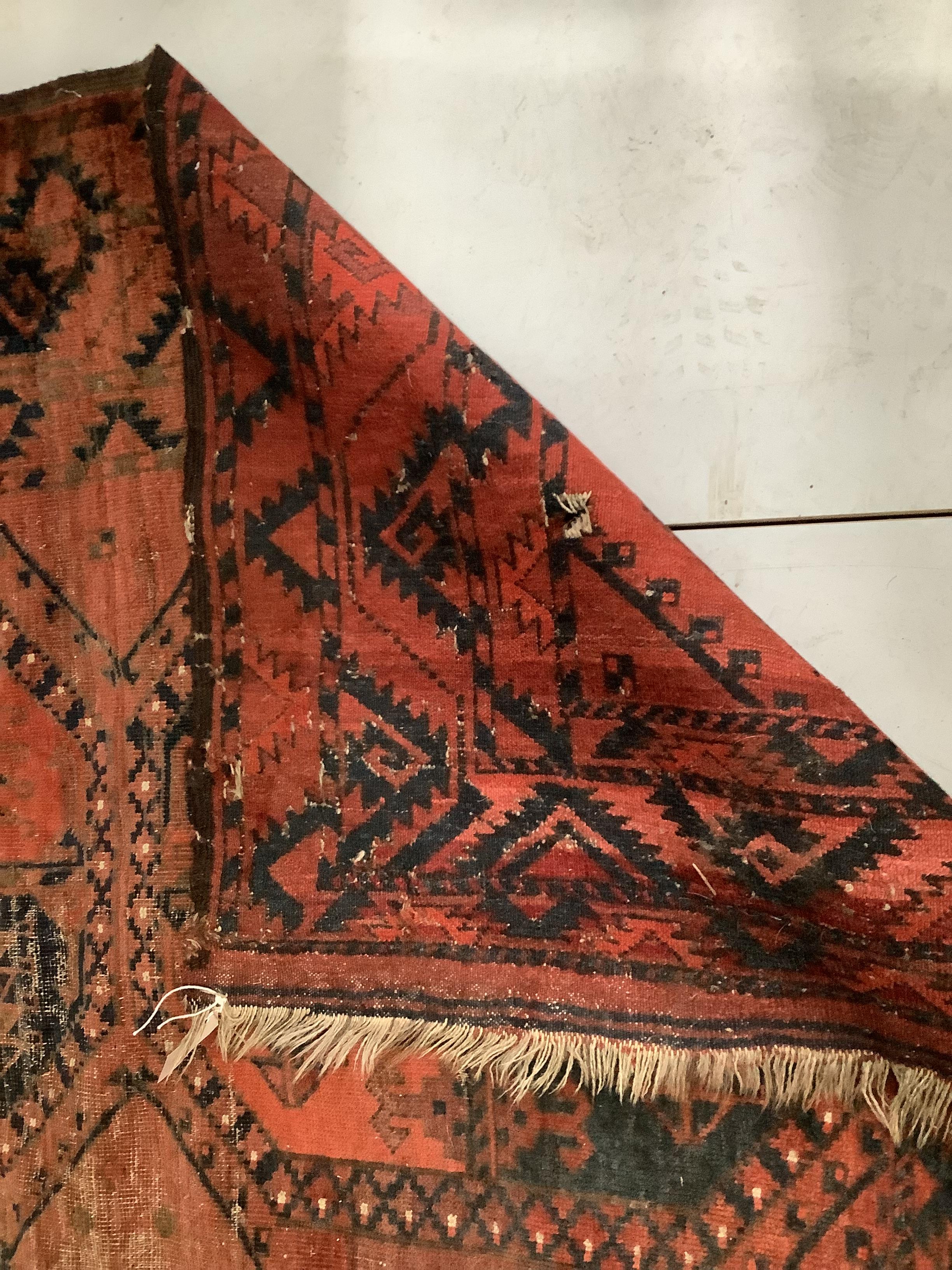 An antique Afghan red ground carpet, 340 x 278cm, worn and holed